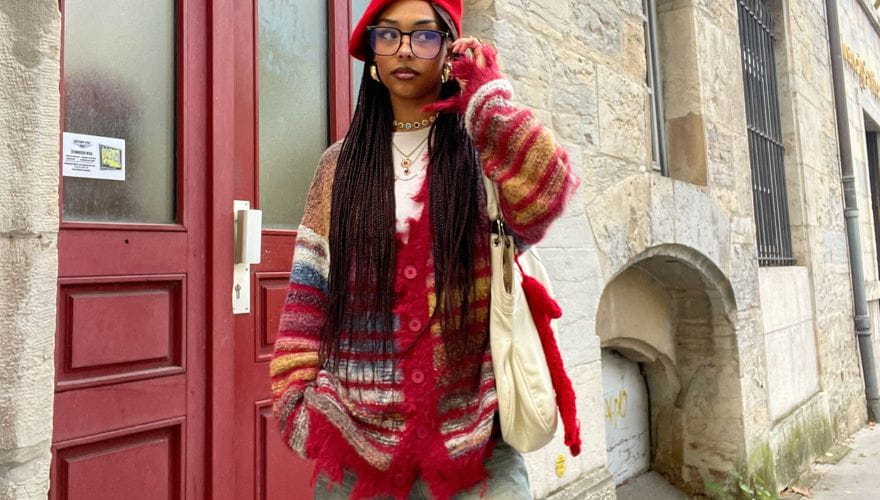 Model styling a striped fuzzy cardigan with red knit layers and light denim